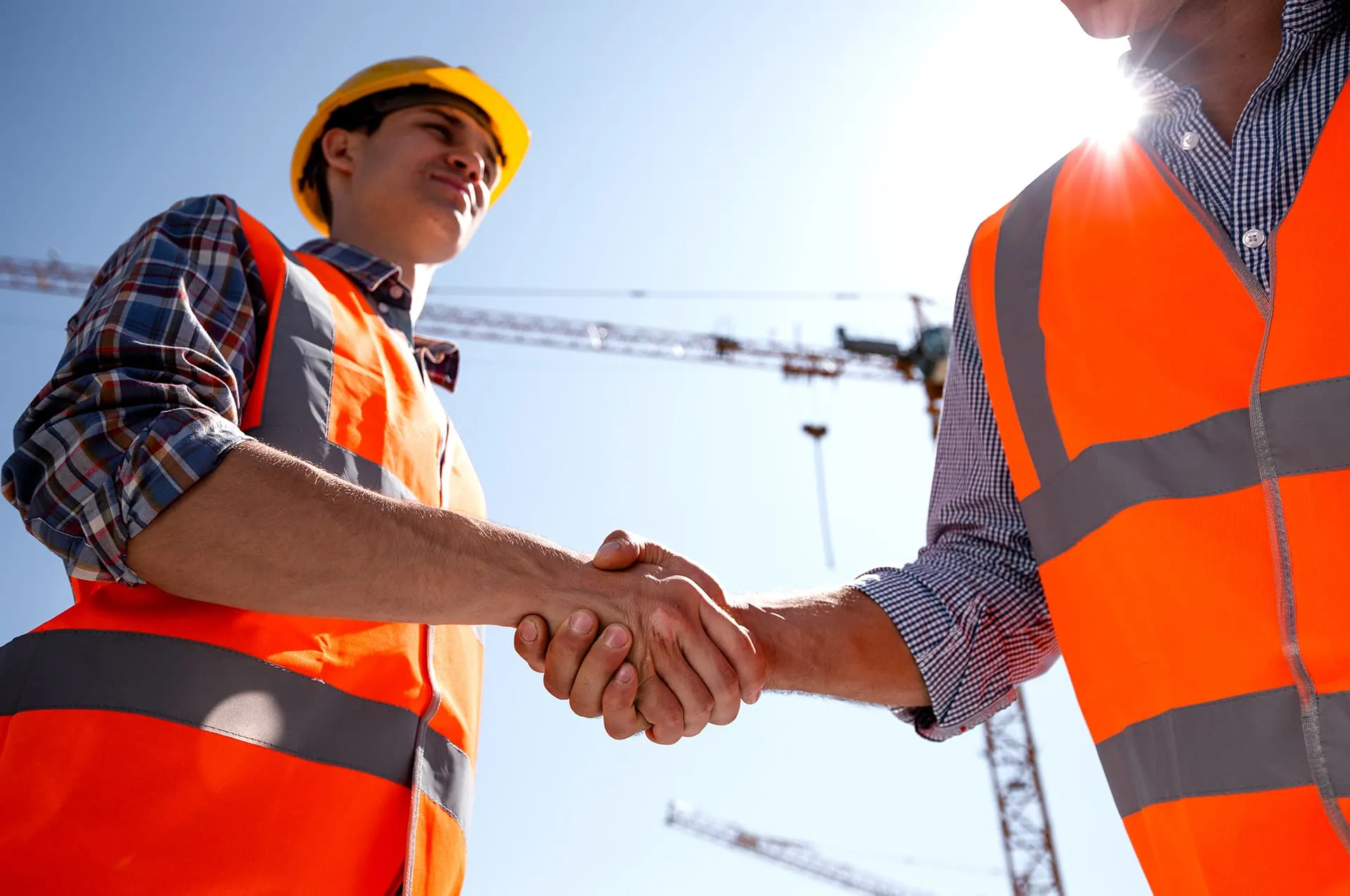 construction workers in high-visibility vests and safety helmets shaking hands at a construction site